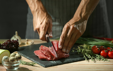 Man cutting raw meat on slate plate in kitchen