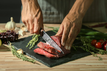 Man cutting raw meat on slate plate in kitchen