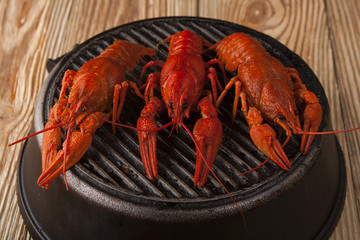 Three red boiled crawfish on black round griddle on wooden background. Food and drinks. Beer snacks