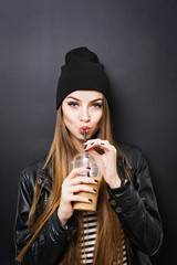 Teenage girl drinking takeaway coffee from a straw, wearing black outfit, against black background