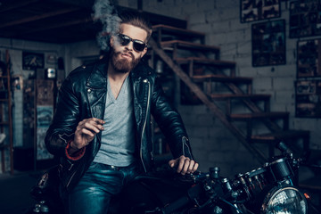 Fototapeta na wymiar Young Bearded Biker in Sunglasses Smoke Cigar.