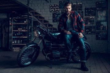 Bearded Biker Sitting on Motorcycle in Garage.