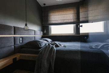 Cozy, dark bedroom interior with gray sheets and blanket and a fancy, upholstered headboard above a comfortable double bed