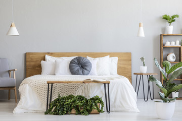 Blue pillow on white bed with wooden headboard in bedroom interior with plants. Real photo - obrazy, fototapety, plakaty