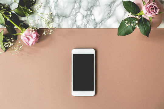 Two pink roses on top view photo of marble table with mockup phone and empty space for your product