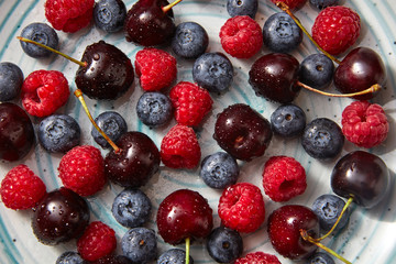 Ripe sweet cherry, raspberry, blueberries with drops of water on them. Natural organic berries close-up background.