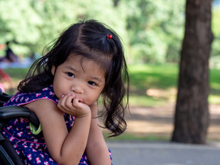 Little asian girl sitting in a stroller at public park. She have be smile and love in sign language.