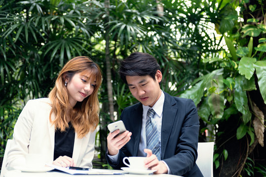 Businessman holding smartphone with businesswoman at outdoor place.