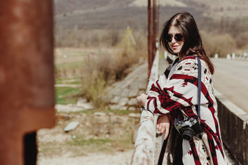 stylish hipster woman relaxing on bridge in fashionable clothes with analog photo camera