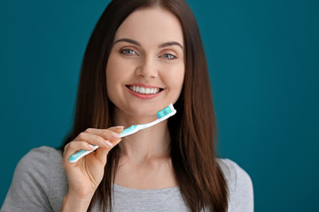 Young woman brushing her teeth on color background