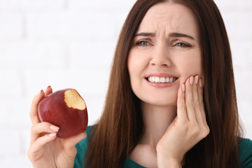 Young woman with sensitive teeth and apple on blurred background