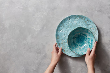 Vintage painted glazed plates dishes on gray concrete table with free space ror text. Girl hold handcraft bowl in her hand. .