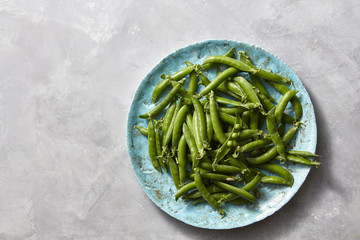 Natural organic green peas in sticks on a blue ceramic plate on a gray marble kitchen table. Top view.