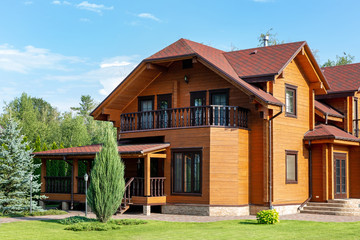 Beautiful luxury big wooden house. Timber cottage villa with with green lawn, garden and blue sky...