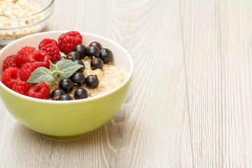 Oatmeal porridge in porcelain bowl with currant berries and raspberries, decorated with mint leaves