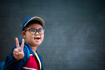 Happy smiling asian boy in glasses showing two fingers as victory sign is going to school for the...