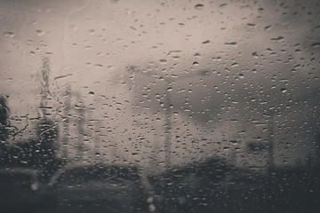 Car window with rain drops on glass or the windshield,Blurred traffic on rainy day in the city,Black and white toned