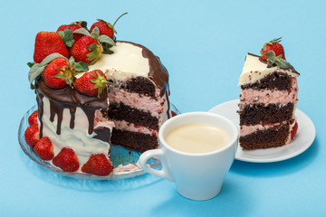 Homemade chocolate cake decorated with fresh strawberries and leaves of mint on glass plate, cup of coffee and piece of cake on white saucer