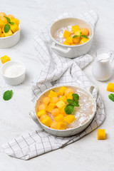 Thai dessert food style : Top view of homemade sago with coconut milk and topping with mango cut into squares and cantaloupe ball in a white bowl  and placed on a marble table with a tablecloth plaid.