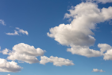 Naklejka na ściany i meble Clear blue sky background with some fluffy white clouds. Vibrant nature scene