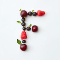 Fruits pattern of letter F english alphabet from natural ripe berries - black currant, cherries, raspberry, mint leaf isolated on a white background.