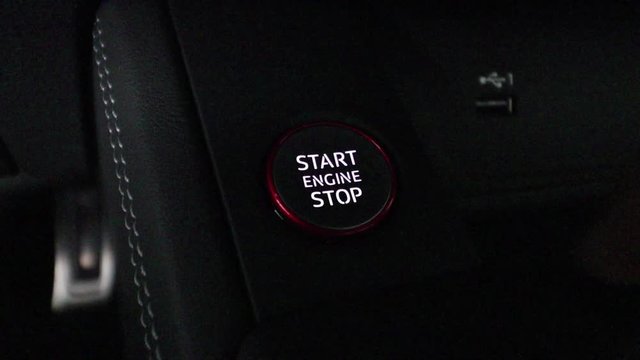 Finger pushing start engine button very dark close up. The button is backlit.