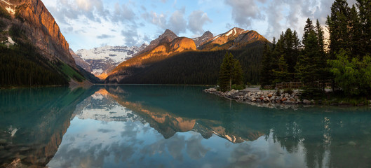 Viewpoint in a glacier lake surrounded by Canadian Rocky Mountains during a vibrant sunrise. Taken in Lake Louise, Banff, Alberta, Canada.