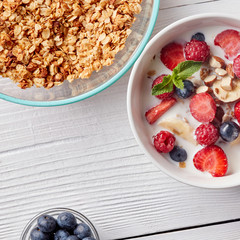 A ready breakfast of natural organic ingredients - granola, berries, nuts, honey, milk for the preparation of natural healthy food on white table.