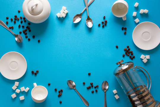 Various coffee making accessories: French coffee press, cups, saucers, coffee beans, spoons and sugar on blue paper background. Good morning concept. Space for copy. Top view. Flat lay