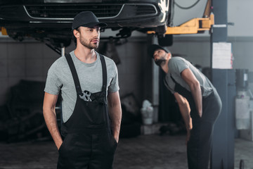Fototapeta na wymiar auto mechanic in overalls with colleague working in workshop behind
