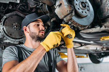 professional mechanic in uniform repairing car without wheel in workshop