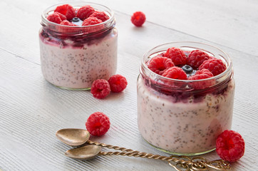 Chia pudding with raspberry in the glass jar on the gray kitchen table decorated with fresh berries...