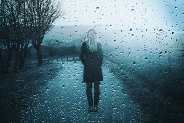 Back view of lonely sad woman standing outdoor with artistic rain drops background.