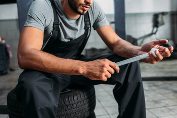 cropped view of professional mechanic holding wrench and sitting in auto repair shop