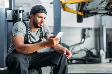 manual worker using smartphone and holding wrench in auto repair shop