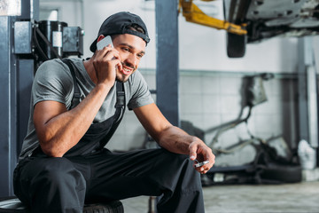 mechanic talking on smartphone and holding wrench in auto repair shop