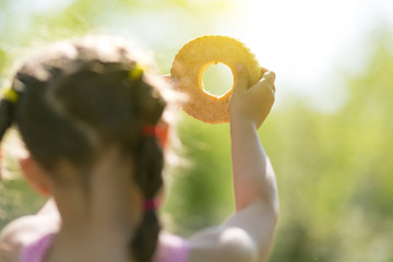 A child is playing with bread in the sun. The girl through the hole in the bread looks at the sun in the sky.