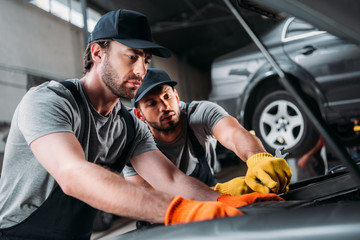 manual workers repairing car in mechanic shop