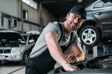 smiling auto mechanic working with car in repair shop