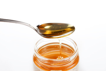 Jar of sweet honey with silver spoon on a white background. Health and beauty concept.