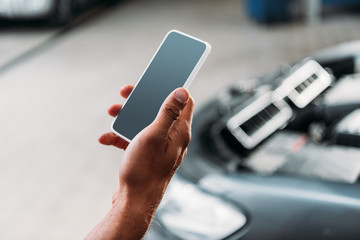 partial view of worker using smartphone with blank screen in mechanic shop