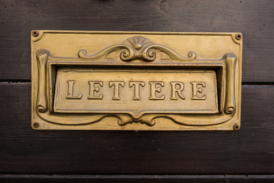 Italian golden plate mailbox with the word letter on a wood wall in the background. Beautiful wallpaper.