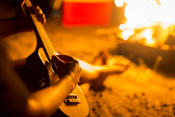 Naklejka premium A person relaxing while sitting next to a campfire on a beach, playing a guitar