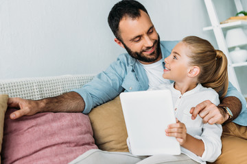 father and daughter using tablet together while sitting on couch at home