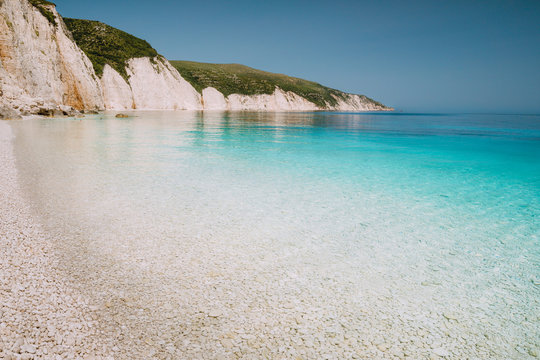 Fototapeta Fteri beach in Kefalonia Island, Greece. One of the most beautiful untouched pebble beach with pure azure emerald sea water surrounded by high white rocky cliffs of Kefalonia