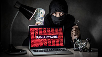 Male hacker holding key and dollar banknote with laptop computer screen showing red binary ransomware attacking with hard disk drive locked. Cyber attack and internet data security concept