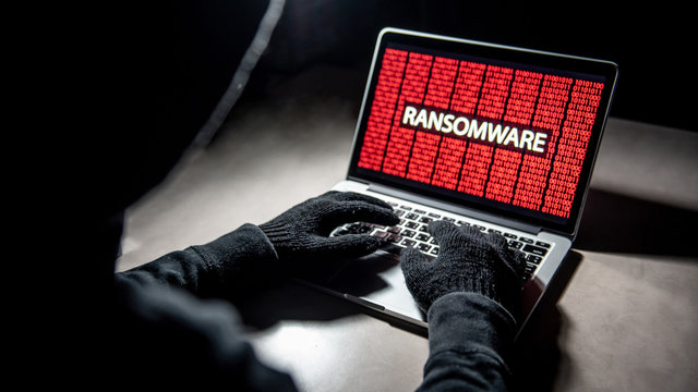 Male Hacker Hand On Laptop Computer Keyboard With Red Binary Screen Of Ransomware Attacking. Cyber Attack And Internet Data Security Concept