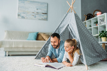 father and daughter lying on floor inside of teepee and reading book together at home © LIGHTFIELD STUDIOS