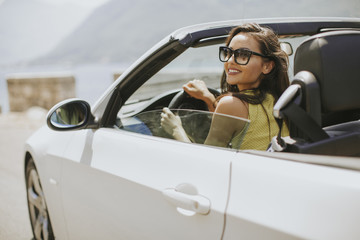 Young woman with sunglasses driving her convertible top automobile on bright sunny day