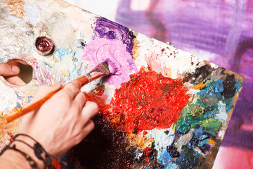 Caucasian hipster artist putting purple paint on his palette in the studio